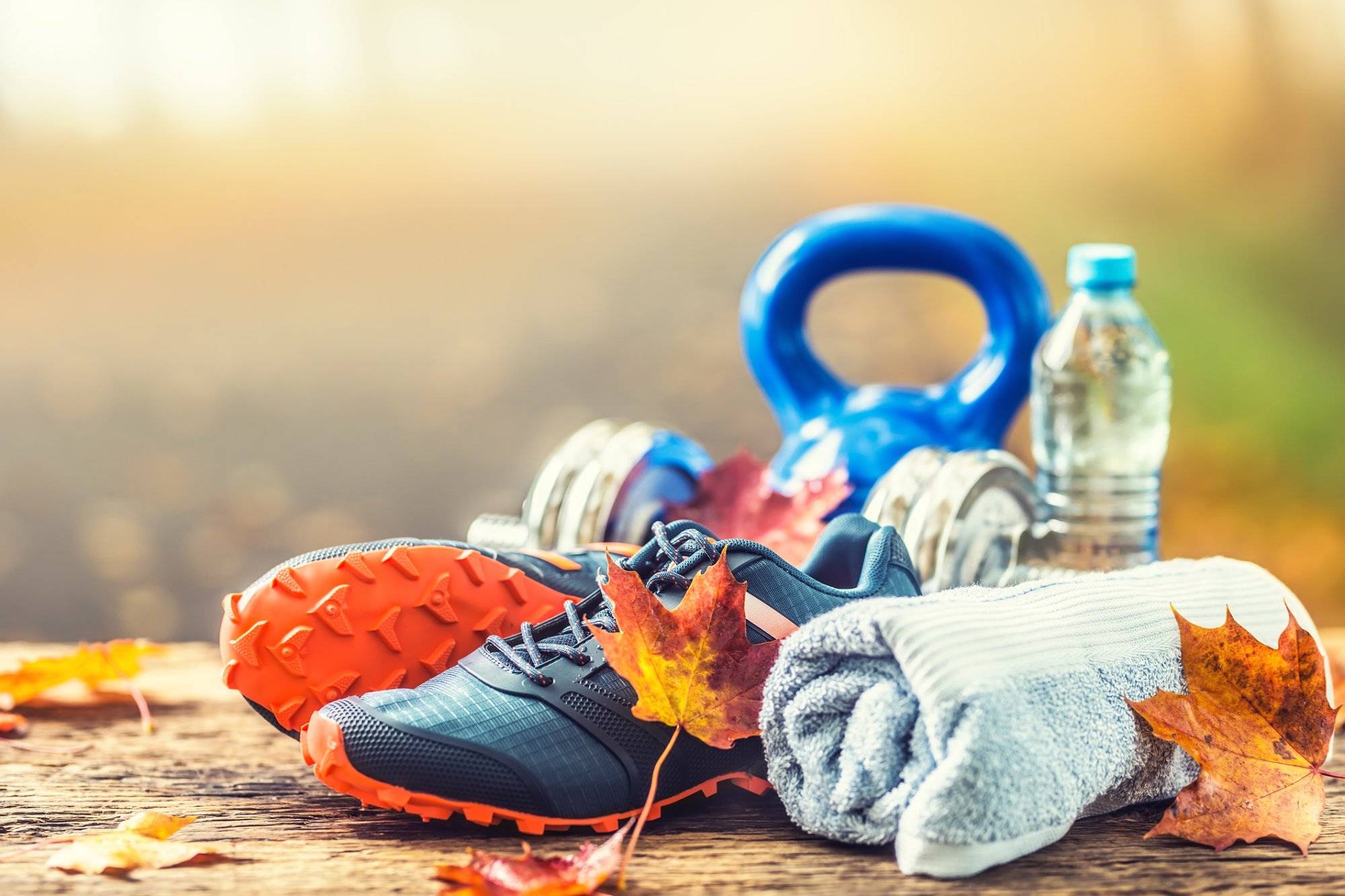 Pair of blue sport shoes water and dumbbells laid on a wooden board in a tree autumn alley with maple leaves – accessories for run exercise or workout activity. Pair of blue sport shoes water and dumbbells laid on a wooden board in a tree autumn alley with maple leaves - accessories for run exercise or workout activity.