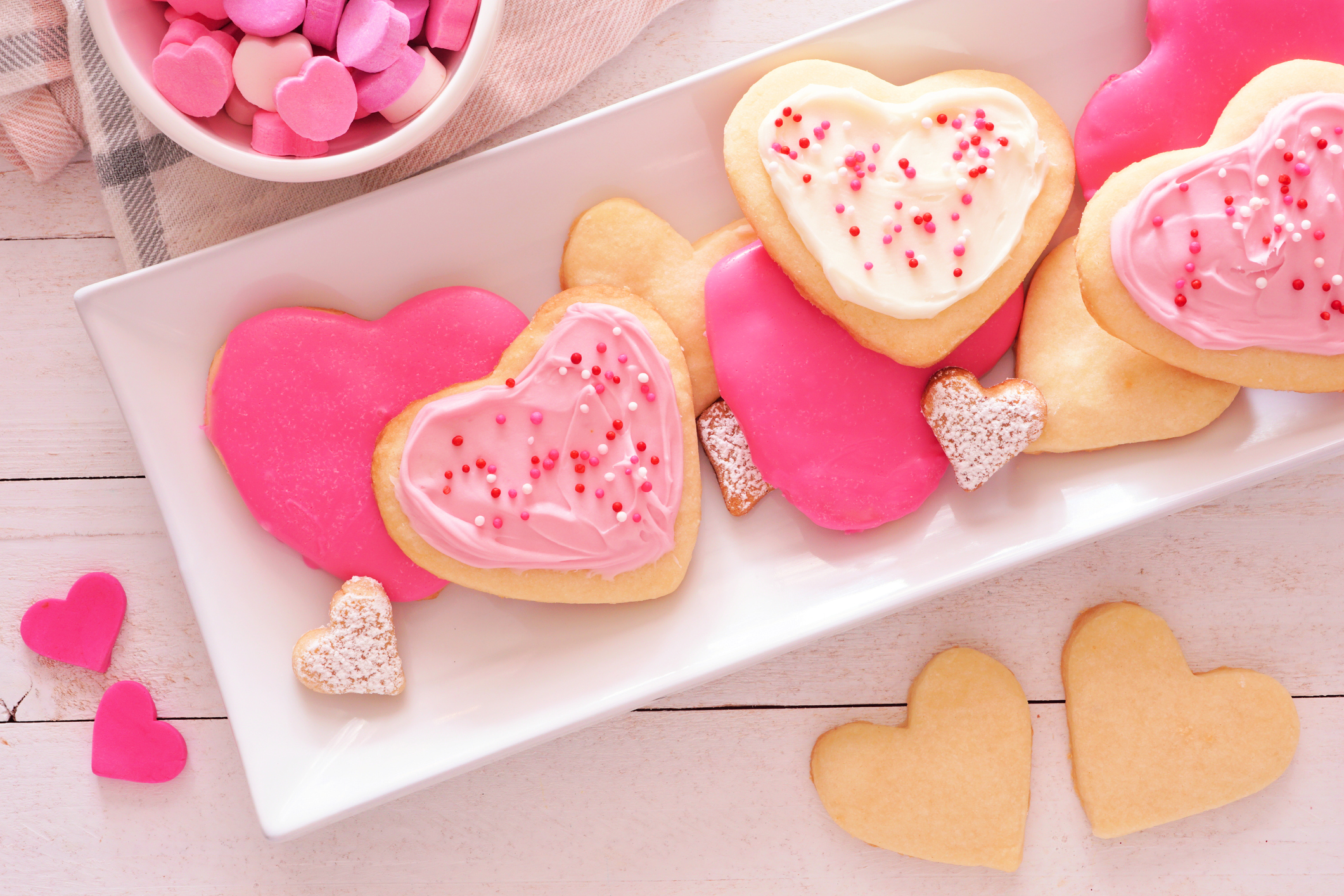 Heart shaped Valentines Day cookies with pink and white icing, overhead on a plate against white wood