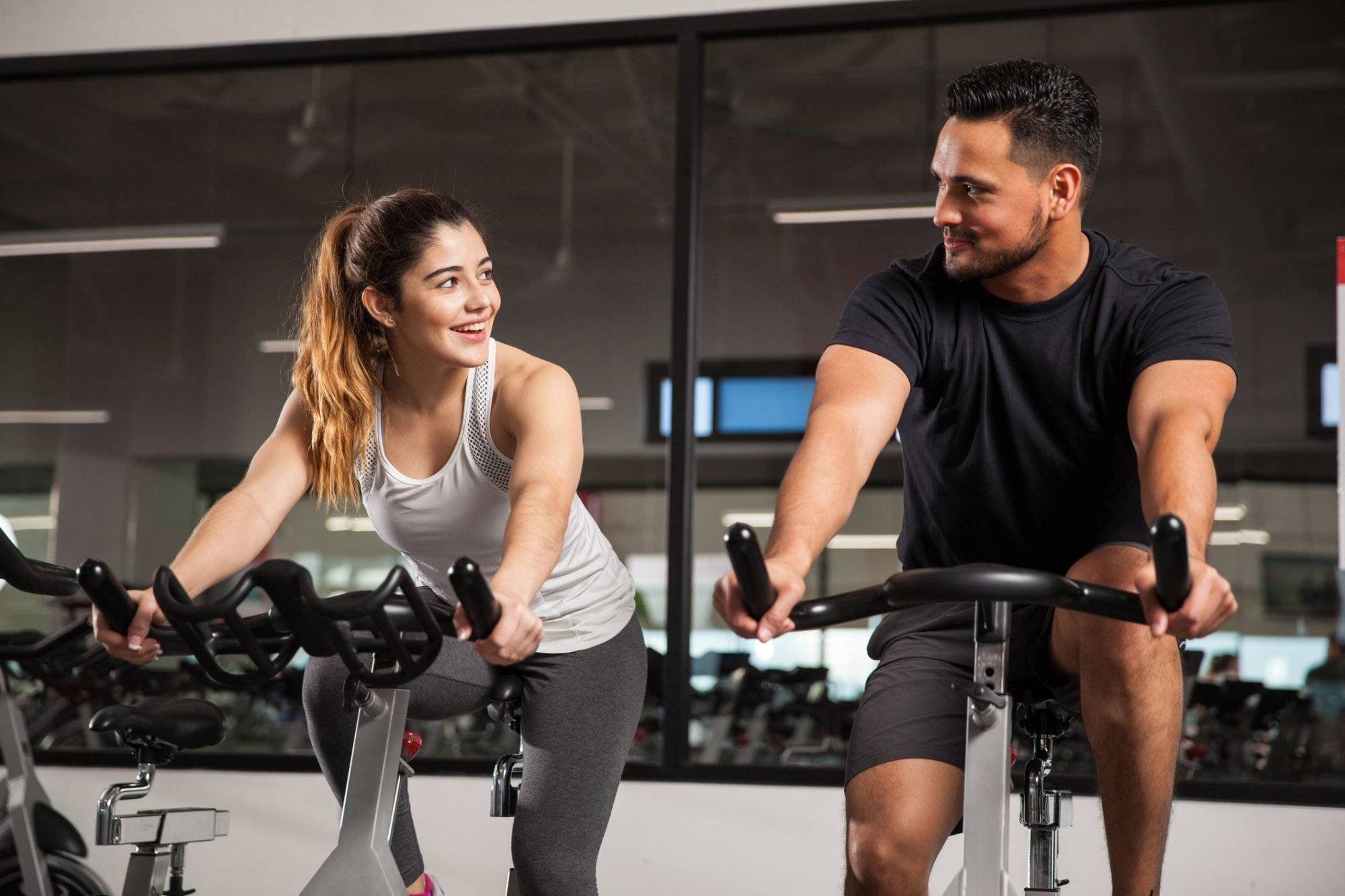 Cute young couple flirting at a gym Beautiful young Hispanic woman flirting and talking to a guy while they both do some exercising at a gym
