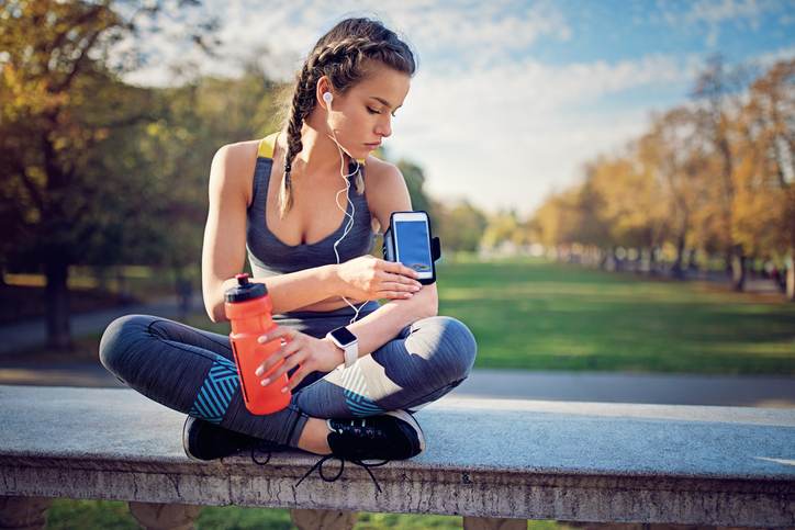 Runner girl is resting and checking her arm band in the park